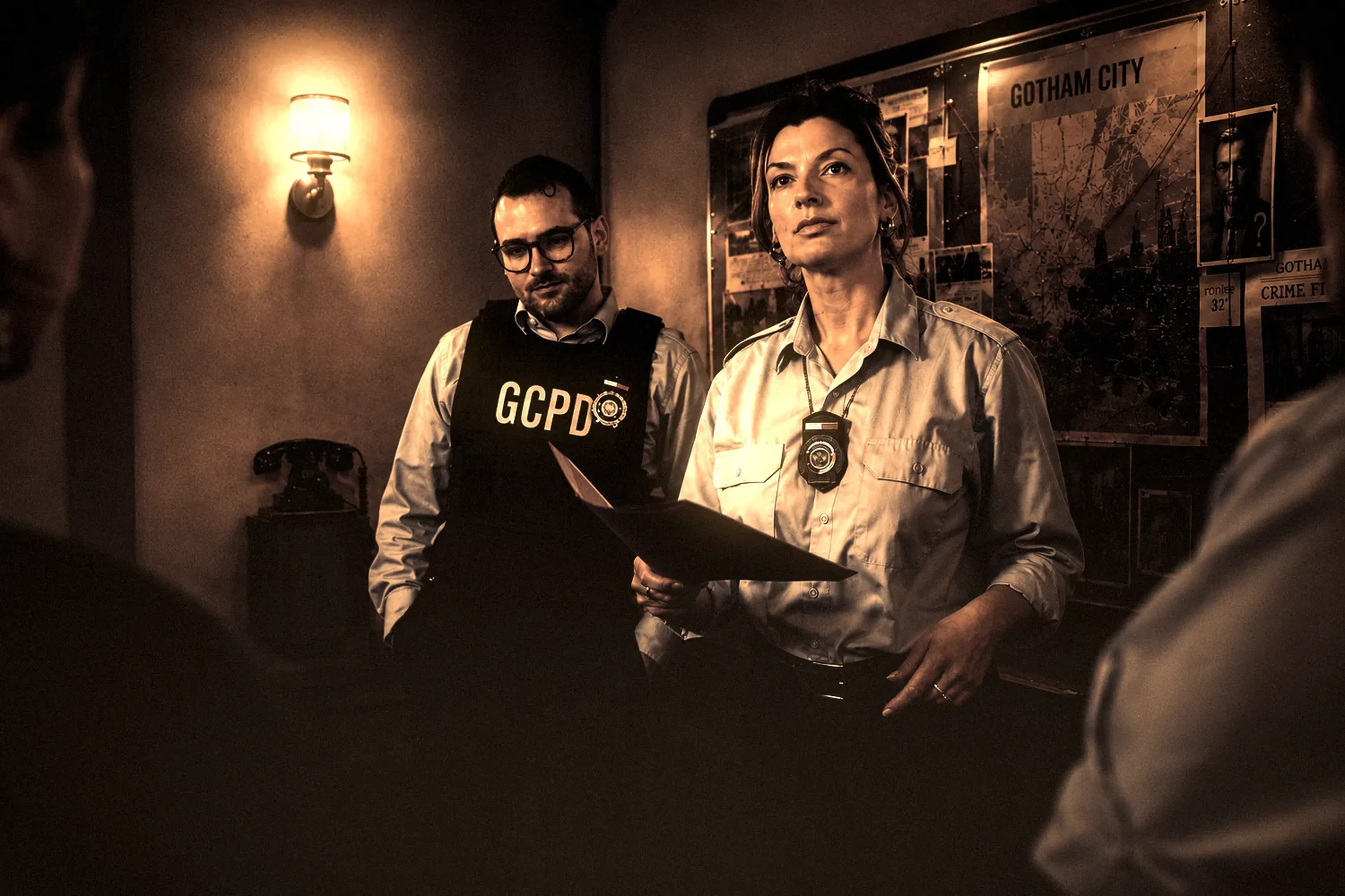 Deux comédiens du GCPD lisent un dossier dans la pénombre chez Batman Escape