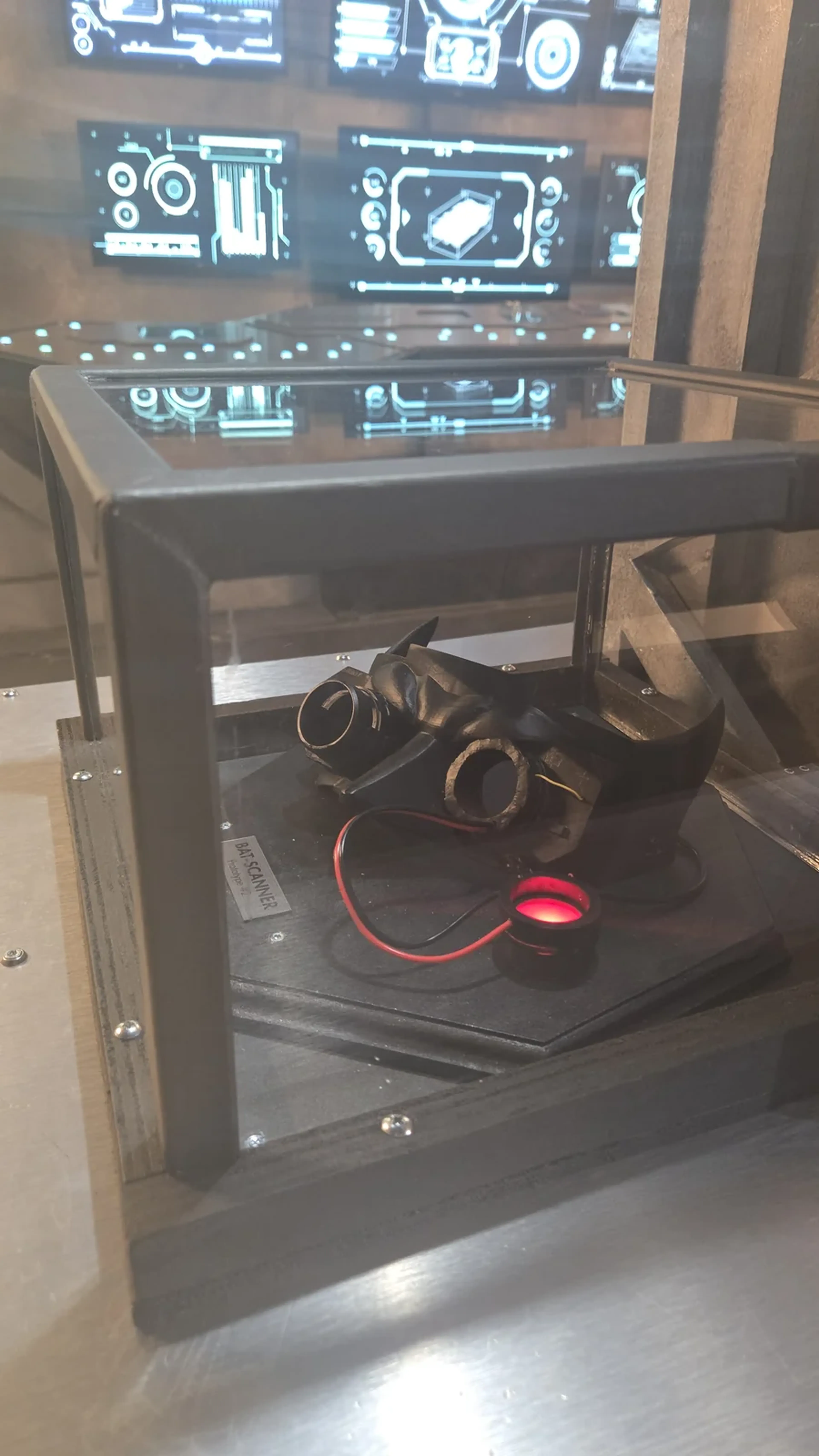 Gadget Bat-Scanner exposé sous vitrine dans le décor high-tech de la Batcave